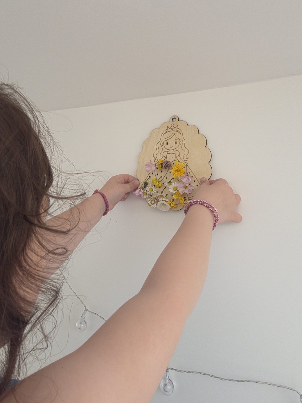 Enfant accrochant fièrement son tableau floral Kidiz'plorer, rempli de fleurs cueillies pendant les vacances d'été, au mur de sa chambre